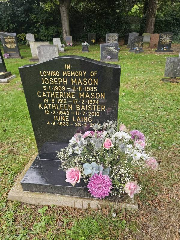 A black granite headstone with pink roses, lilac chrysanthemums, sea holly and gypsophila arranged at its base
