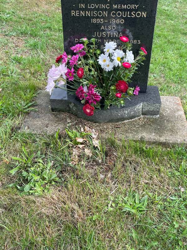 A black granite headstone with pink, white and red asters and chrysanthemums in the vase at its base