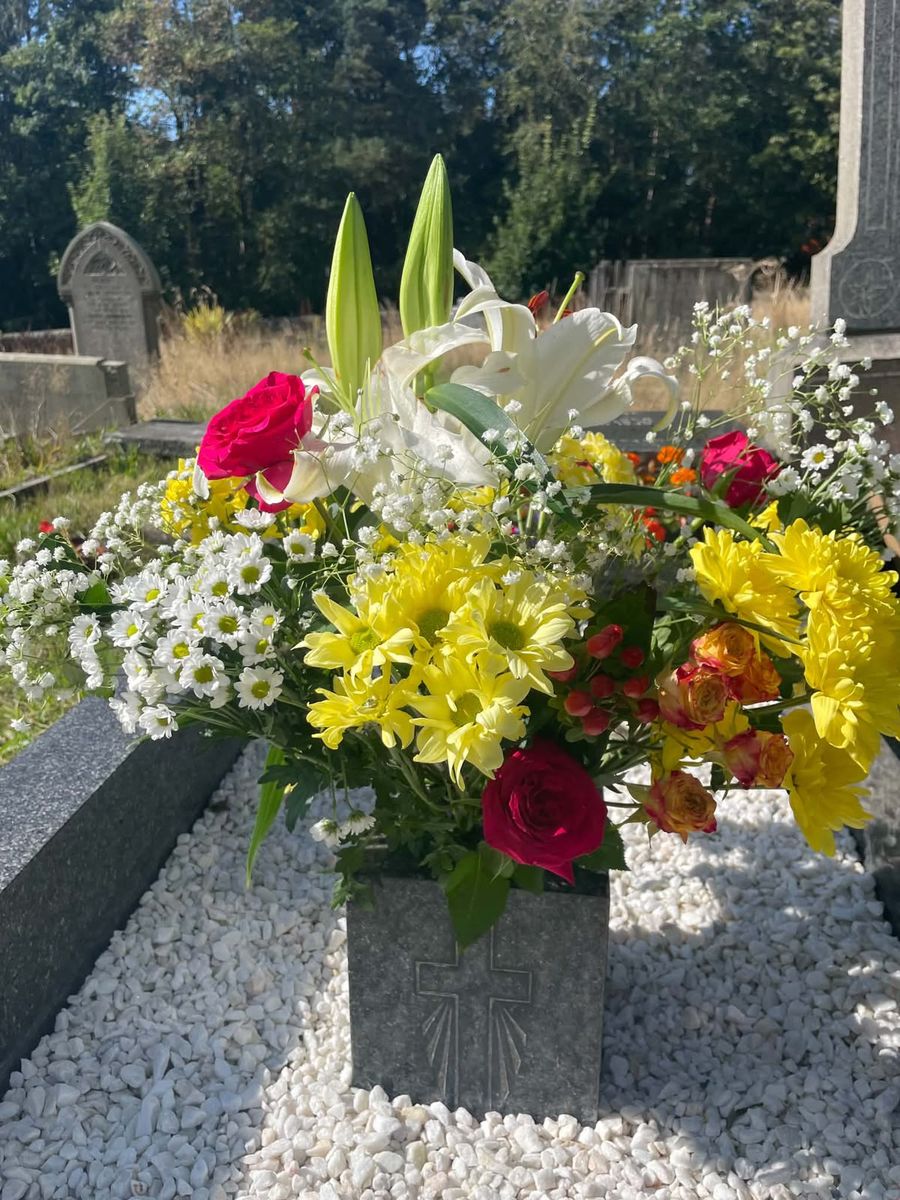 White lilies, yellow chrysanthemums, red roses and gypsophila in a stone vase on a grave of white gravel