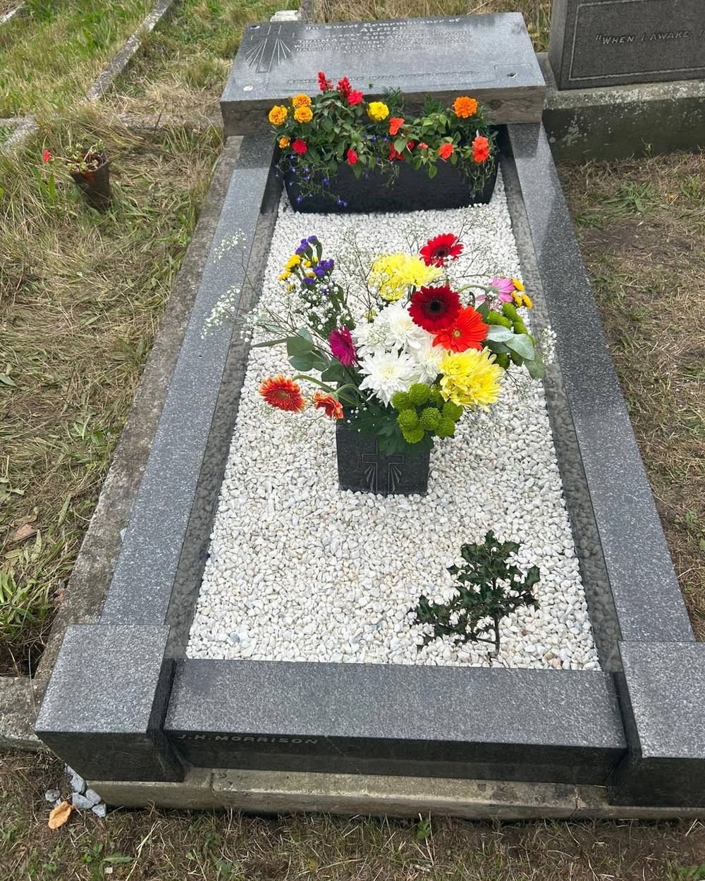 The same grave after care, with clean white gravel, a planted trough and fresh flowers